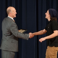 Doctor Potteiger shaking hands with an award recipient in a black shirt and a beanie
